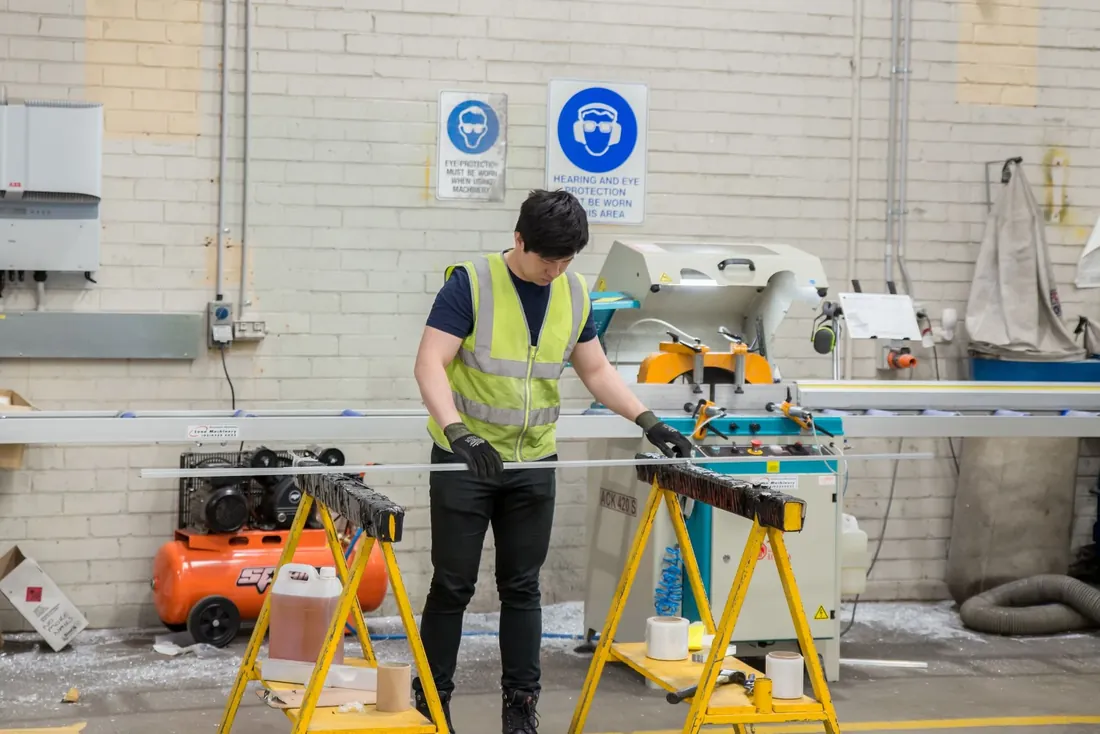Two sign fitters cutting a length of trim on a saw bench