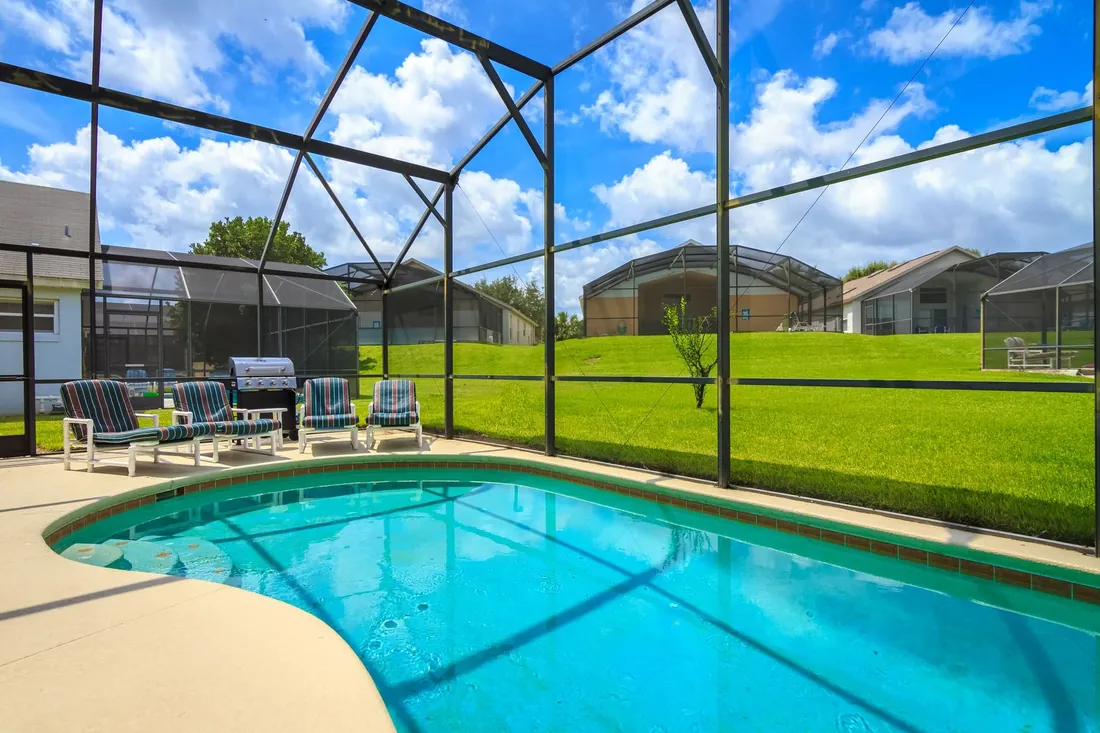 A pool inside a screen enclosure with chairs and a lawn beyond