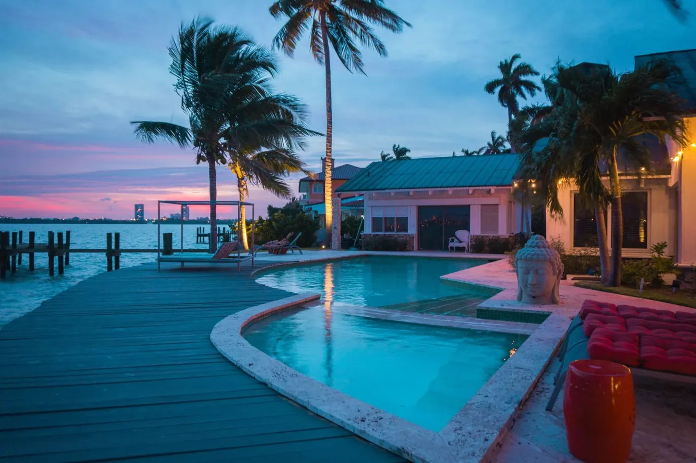 A pool on a waterfront deck at dusk with palm trees