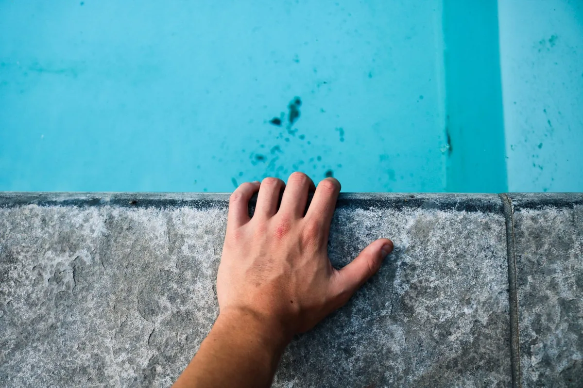 A hand on pool coping beside a dirty waterline