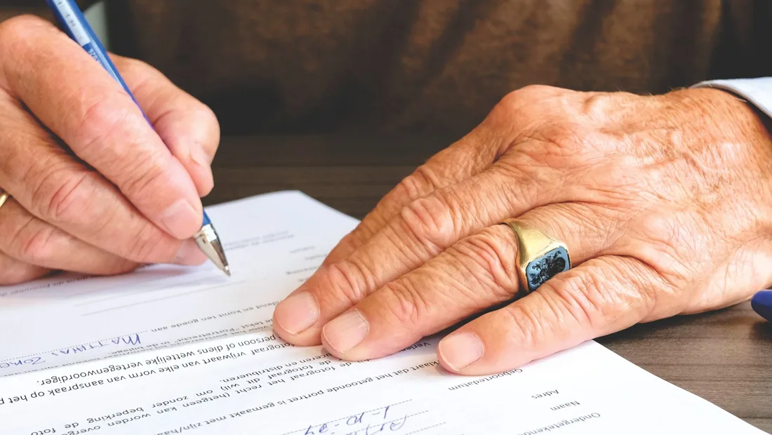 An older hand signing a mortgage document