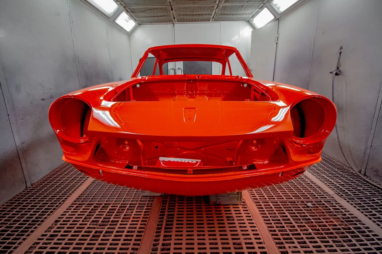 A car body shell freshly painted orange in a spray booth