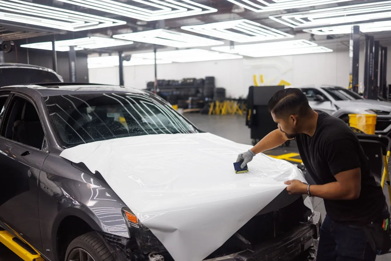 A fitter smoothing white wrap film over the front of a grey car