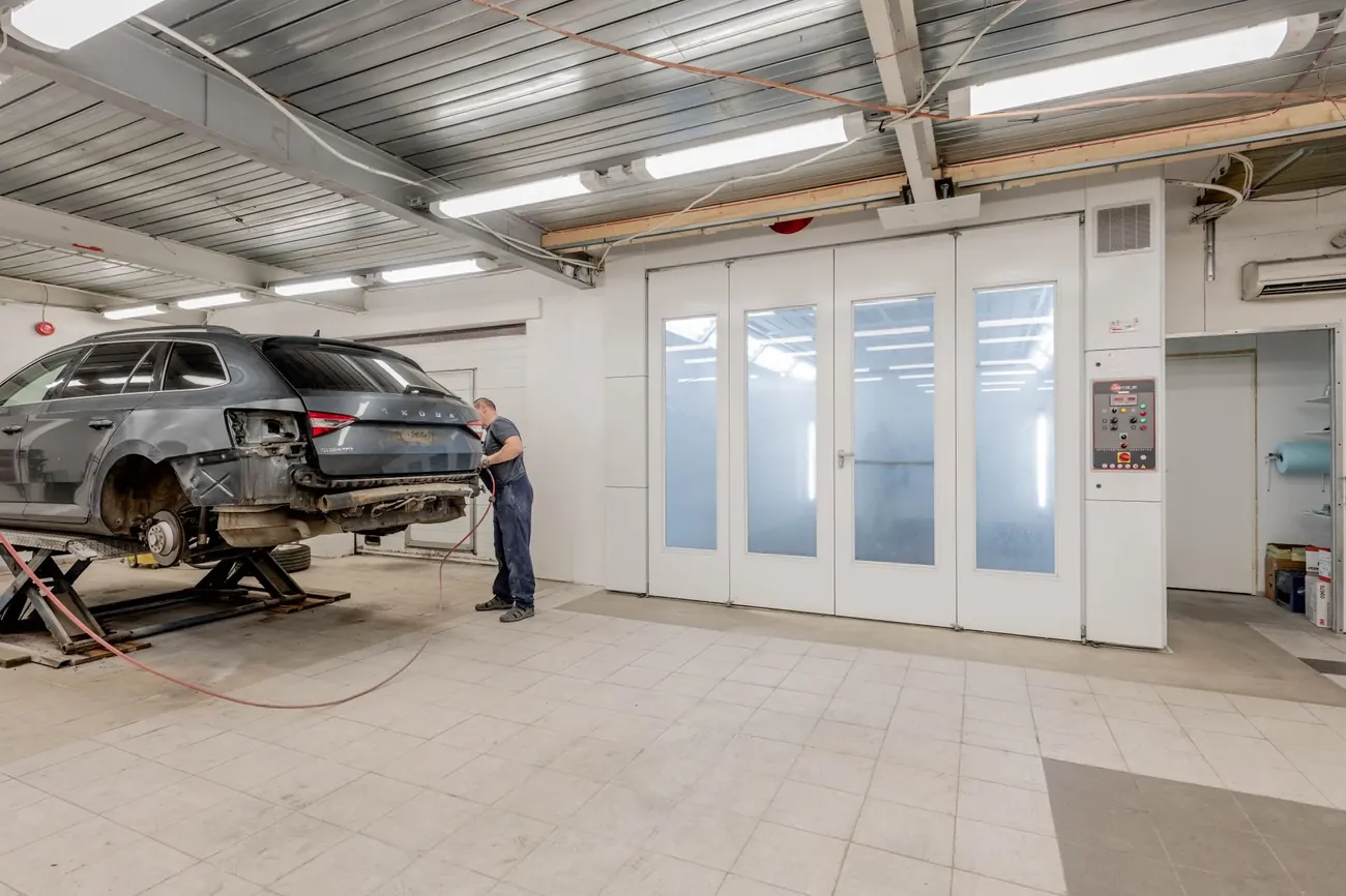 A car on a lift in a bright body shop next to the spray booth
