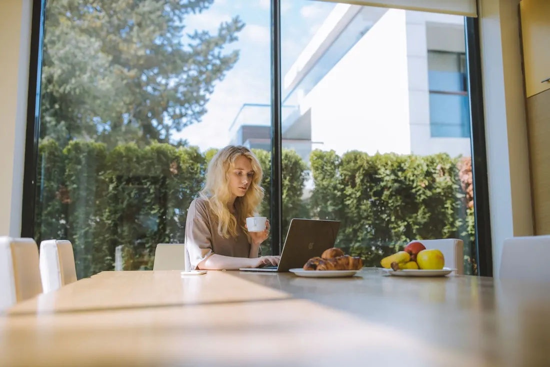 A woman with a coffee at a table in a glass fronted garden room