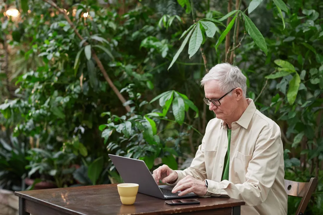 A man working on a laptop in a garden office full of plants