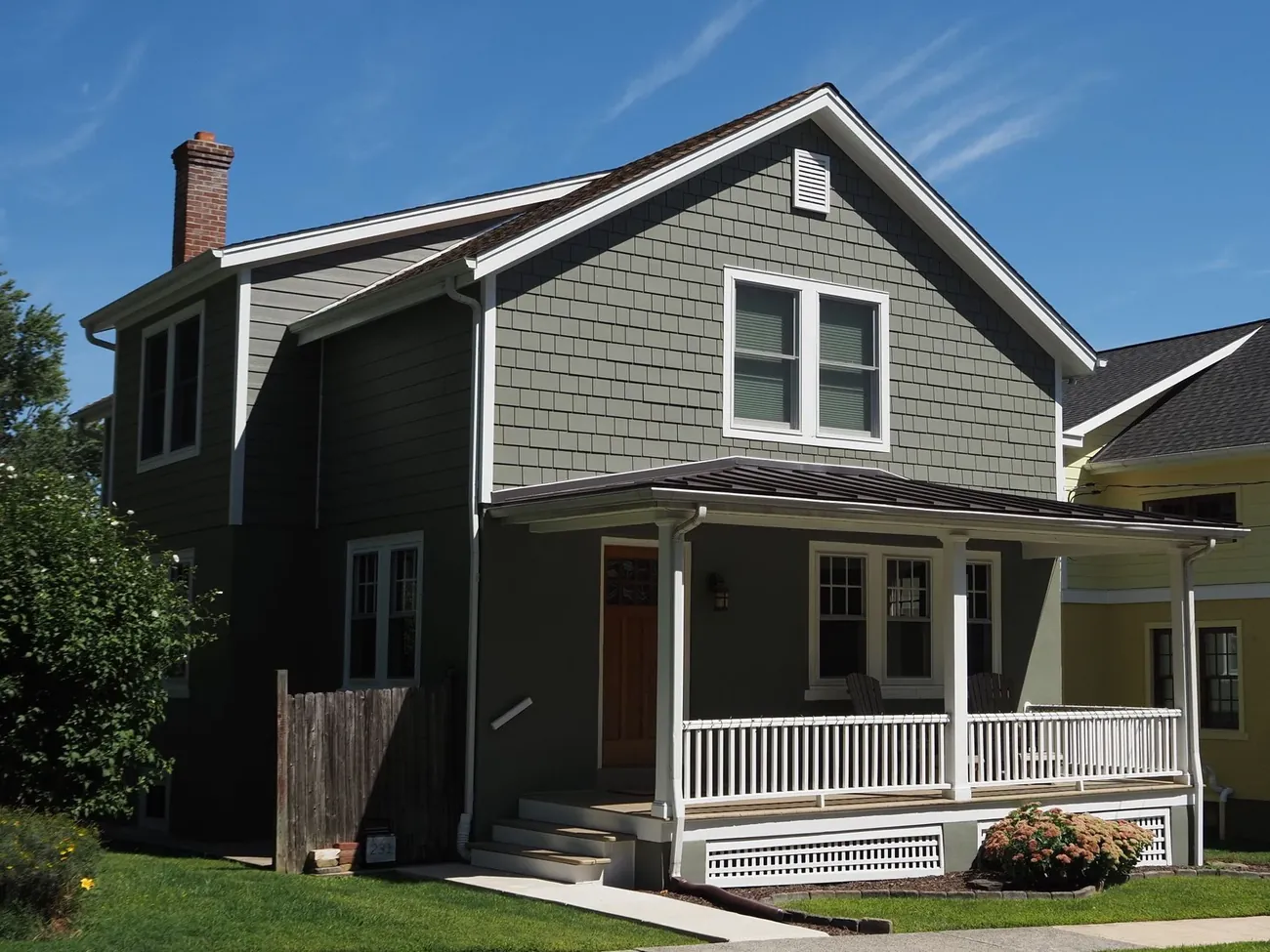 A two story house in gray green siding with shakes up high, white trim and a white porch rail