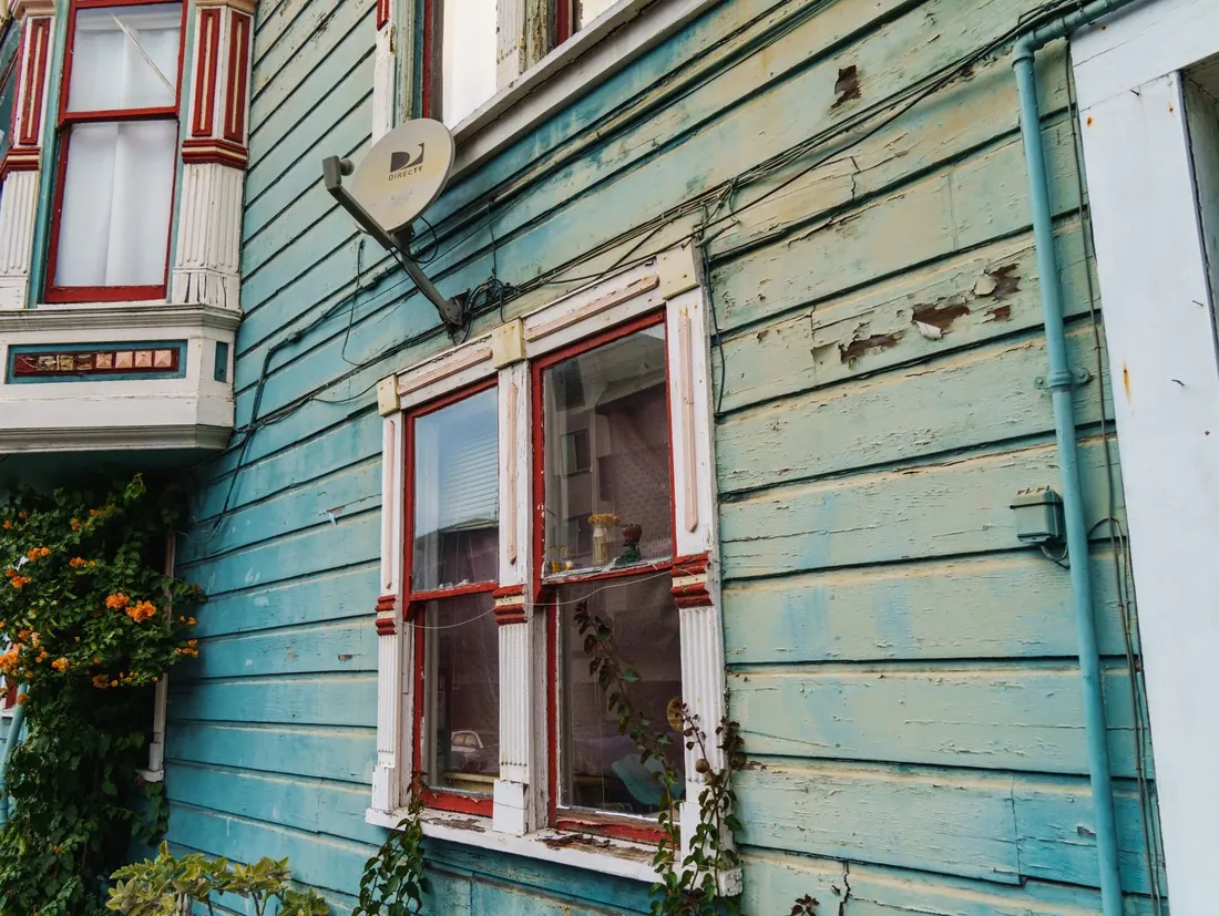 Old wooden siding with peeling blue paint around a window