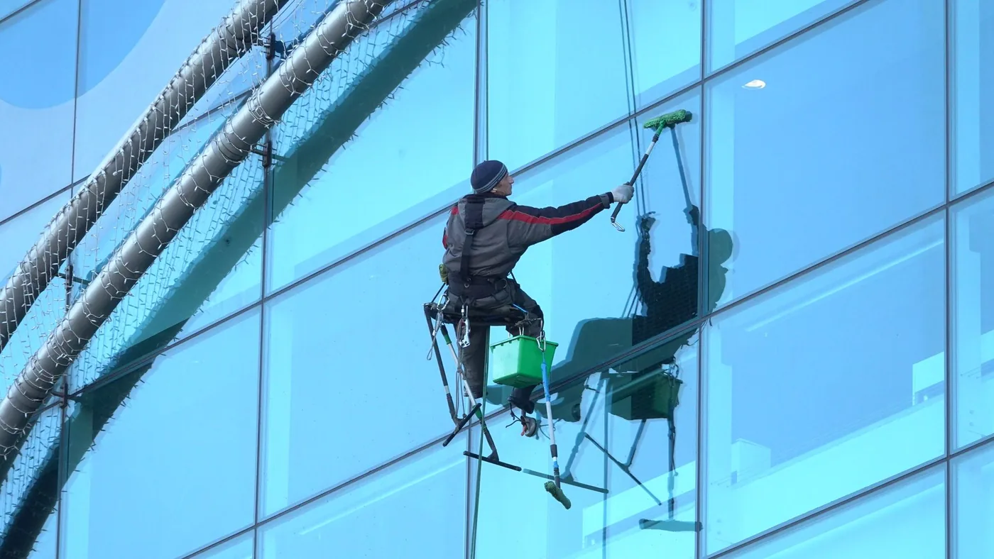 Cleaner working a glass office facade from a cradle