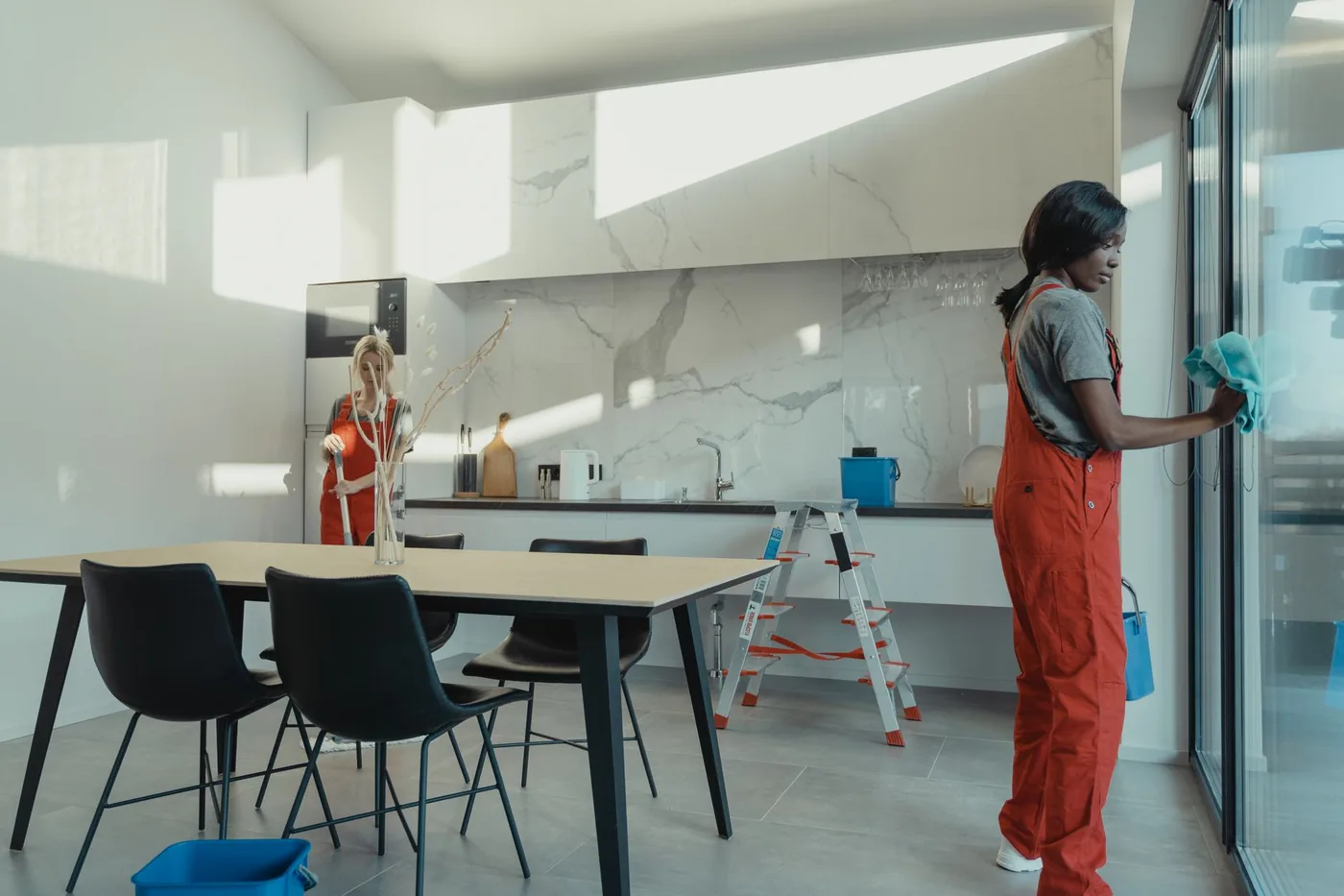 Two cleaners working full height glass in a bright kitchen