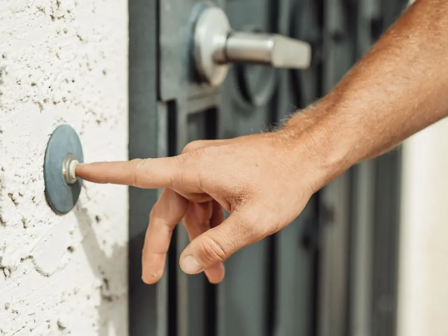 A finger pressing a doorbell by a front door