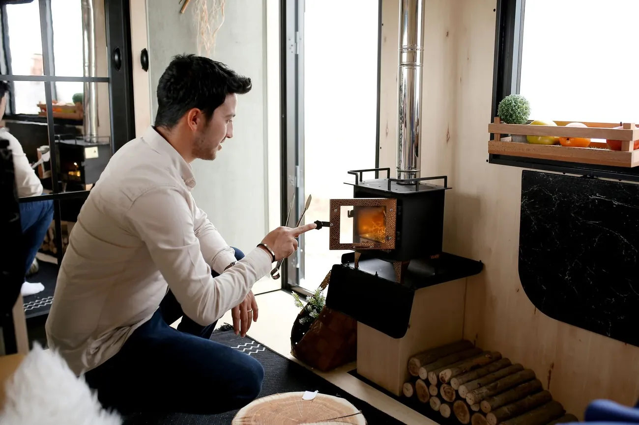A man lighting a small wood stove in a bright room