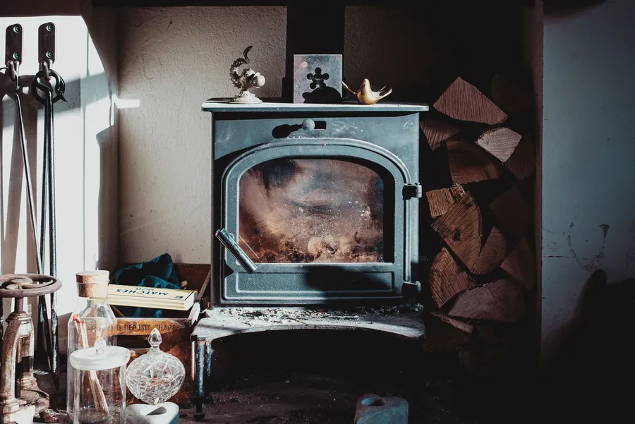 A traditional cast iron stove with logs stacked beside it
