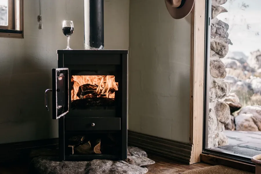 A compact stove burning with its door open and a glass of wine on top
