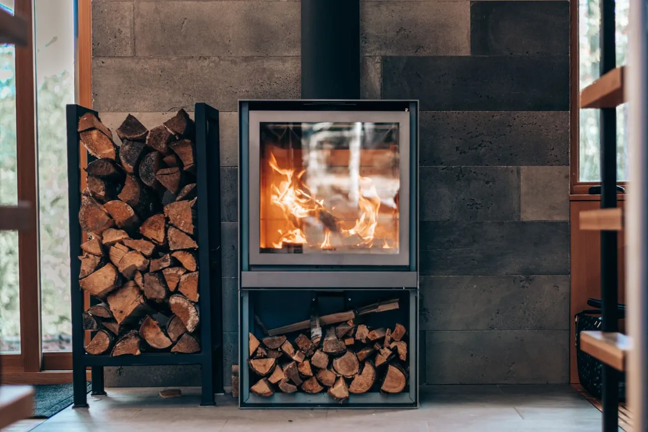 A modern wood stove burning beside a tall log store