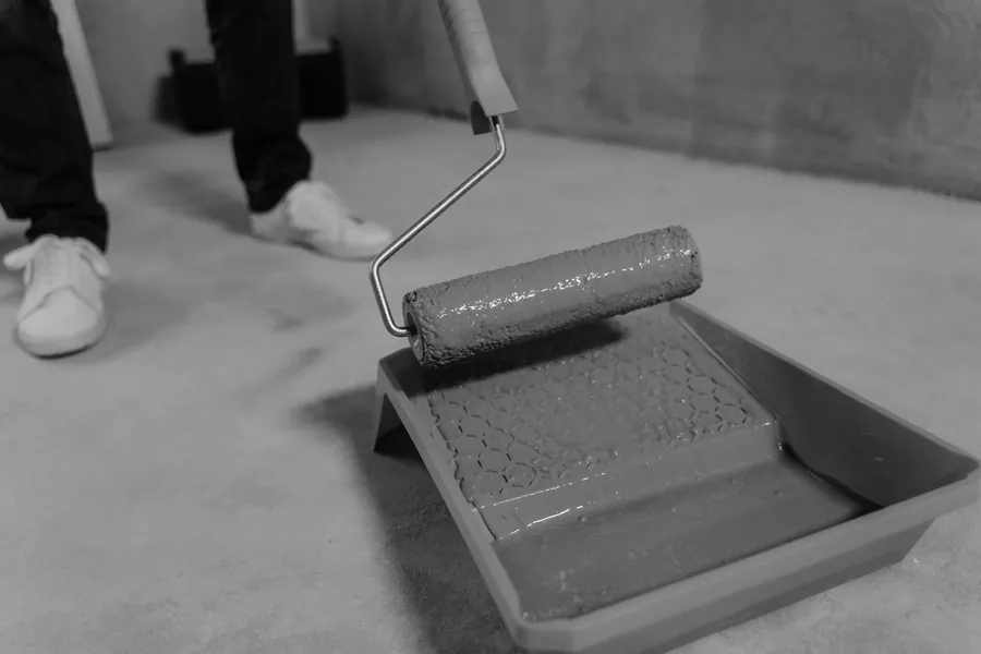 A paint roller resting in a tray on a bare concrete floor
