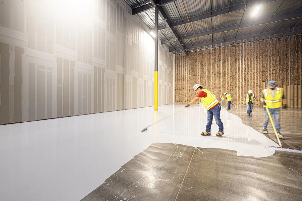 A crew in hi vis spreading white coating across a large warehouse floor