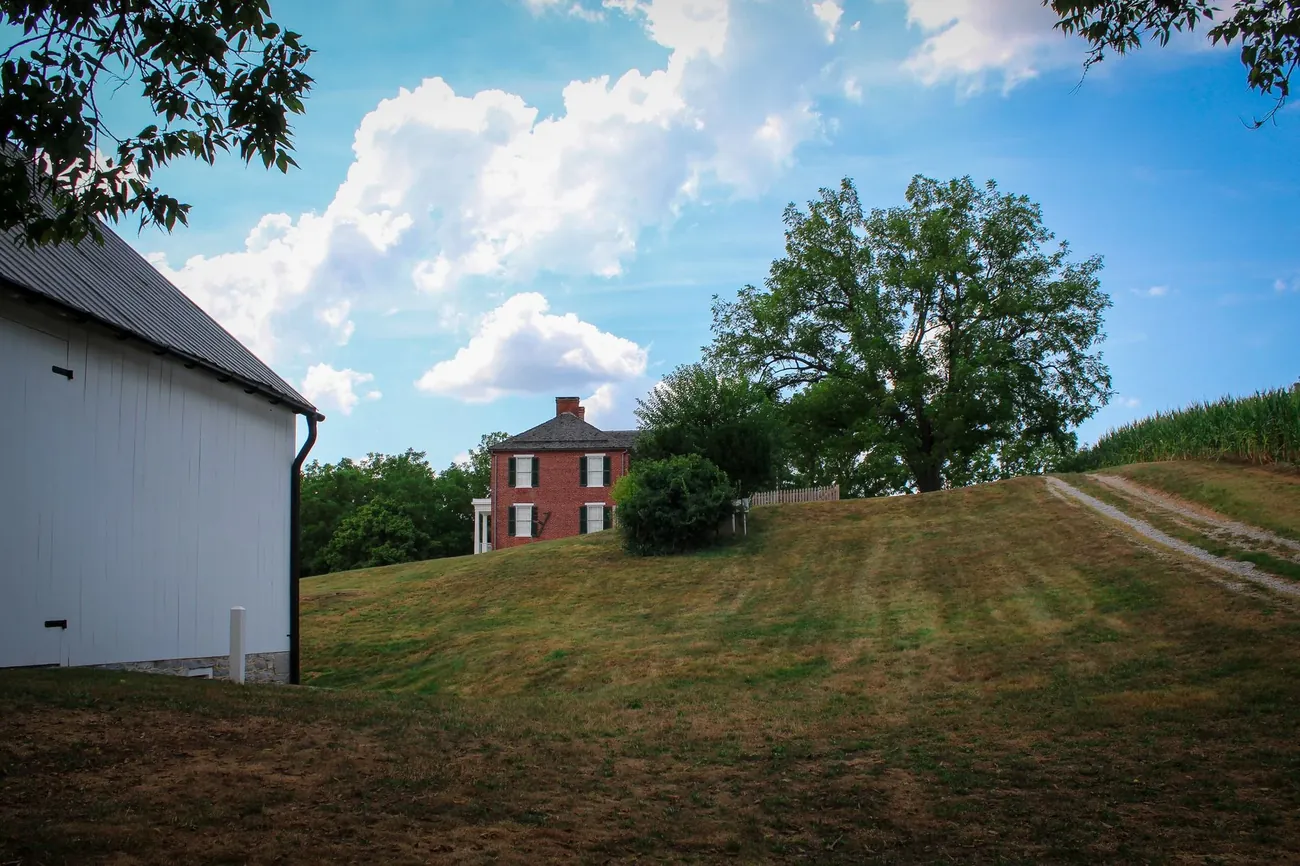 A red brick farmhouse beside a white barn on a green hill