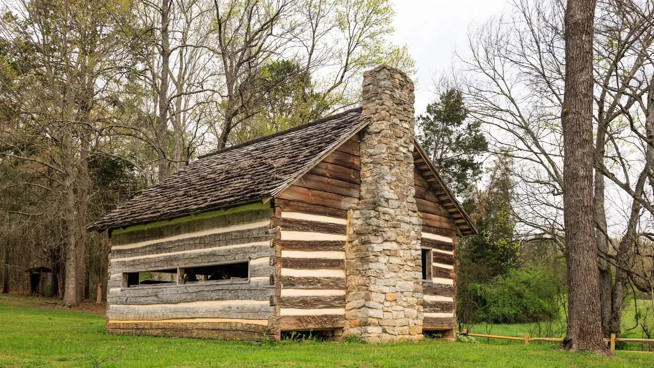 A log cabin with a stone chimney among trees