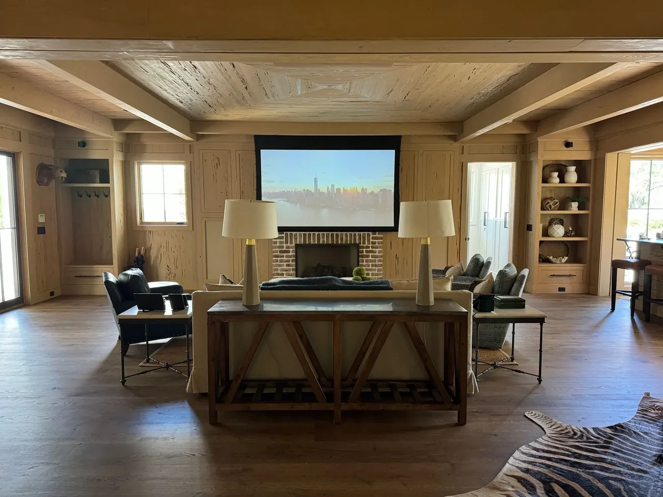 A timber lounge with a projector screen above the fireplace and armchairs around a long table