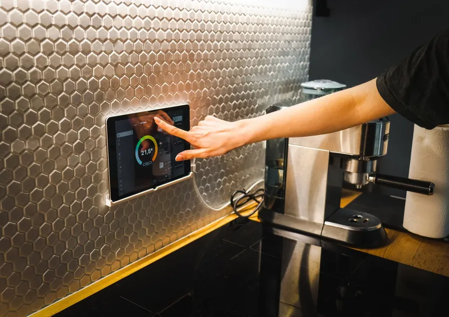 A hand pressing a touch panel set into a tiled kitchen wall