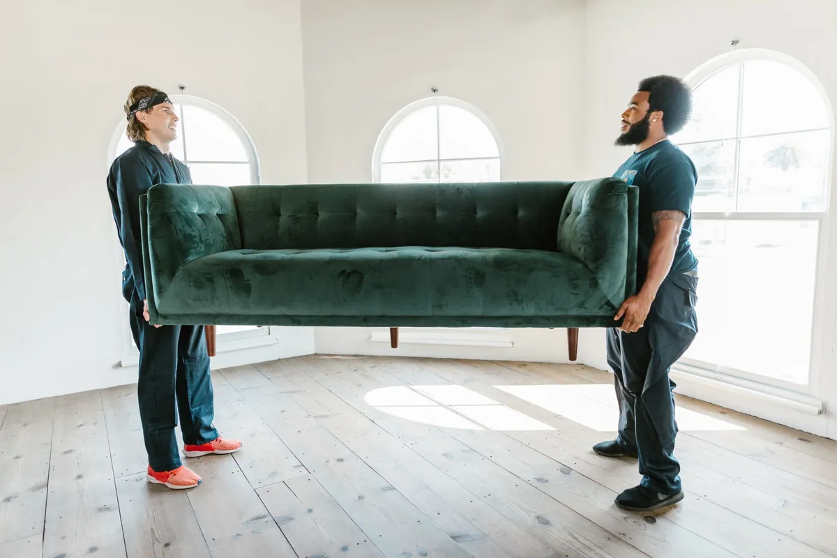 Two crew members carrying a sofa out of a room