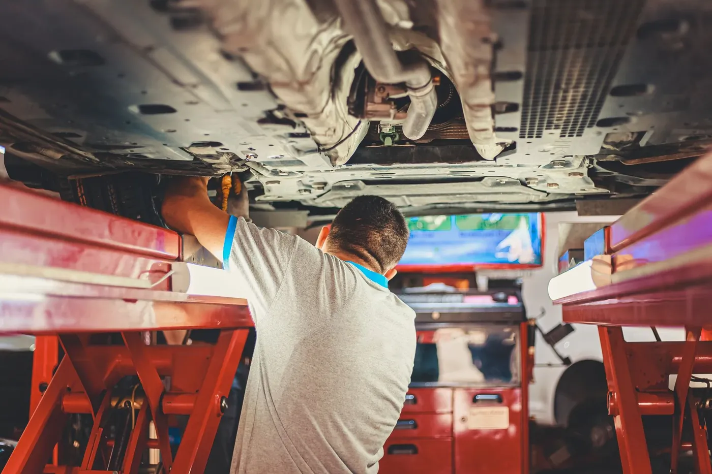 A mechanic working under a car raised on a red lift