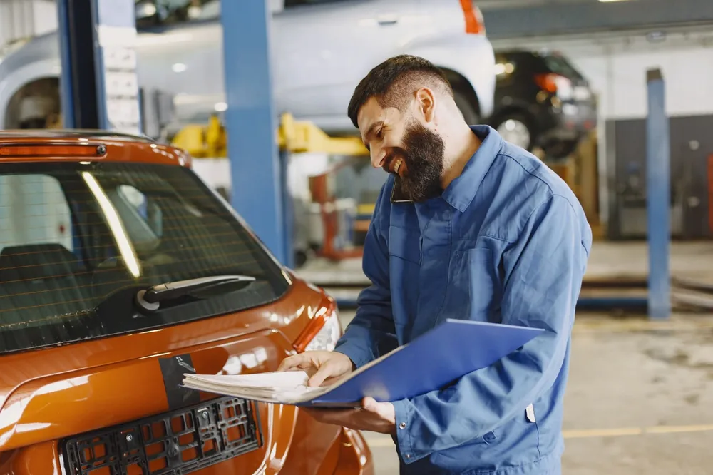A mechanic writing up a job sheet by an orange car