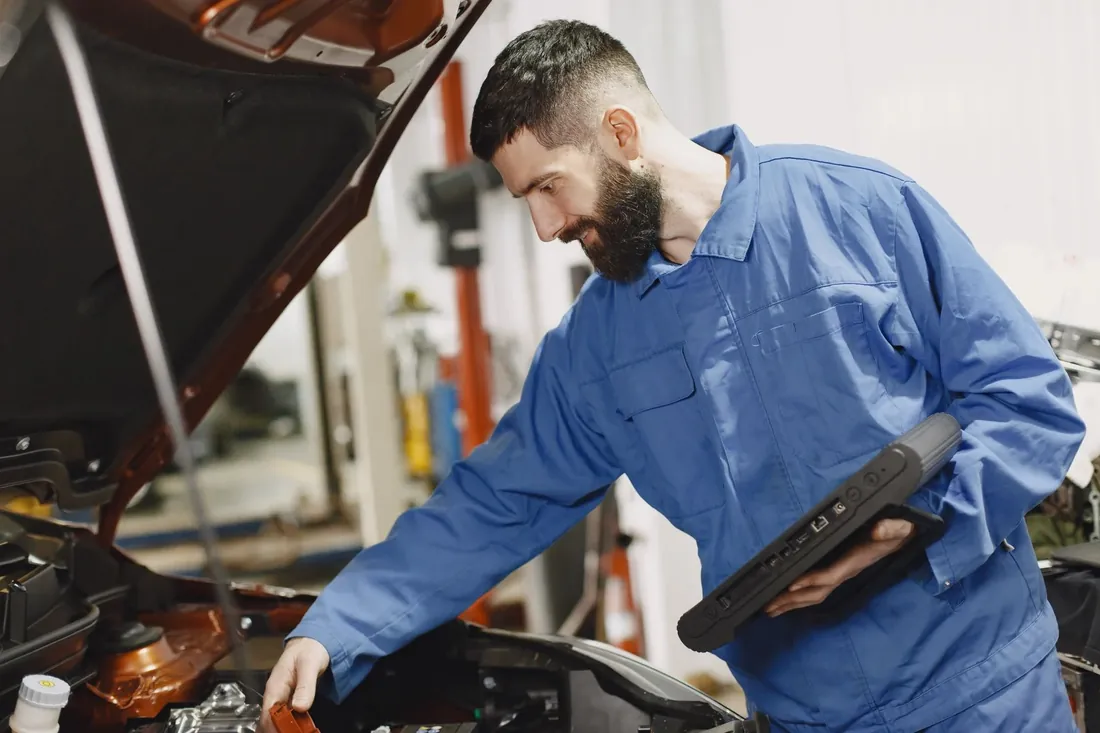 A technician with a diagnostic tablet at an open bonnet