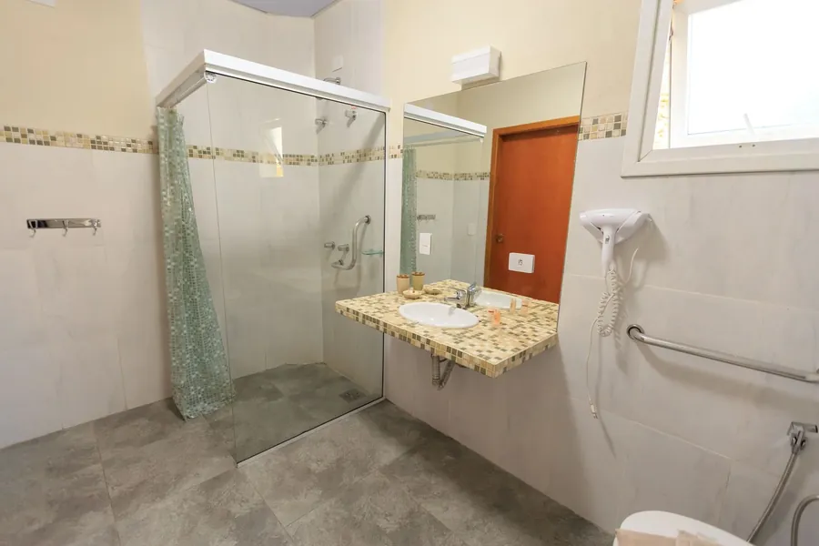 A bright bathroom with grab rails beside the basin and the shower