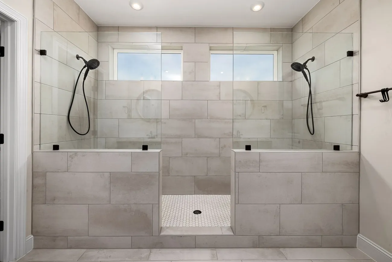 A large walk in shower with two shower heads and pale grey tiles