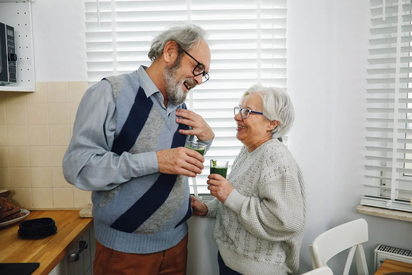 An older couple laughing together in their kitchen