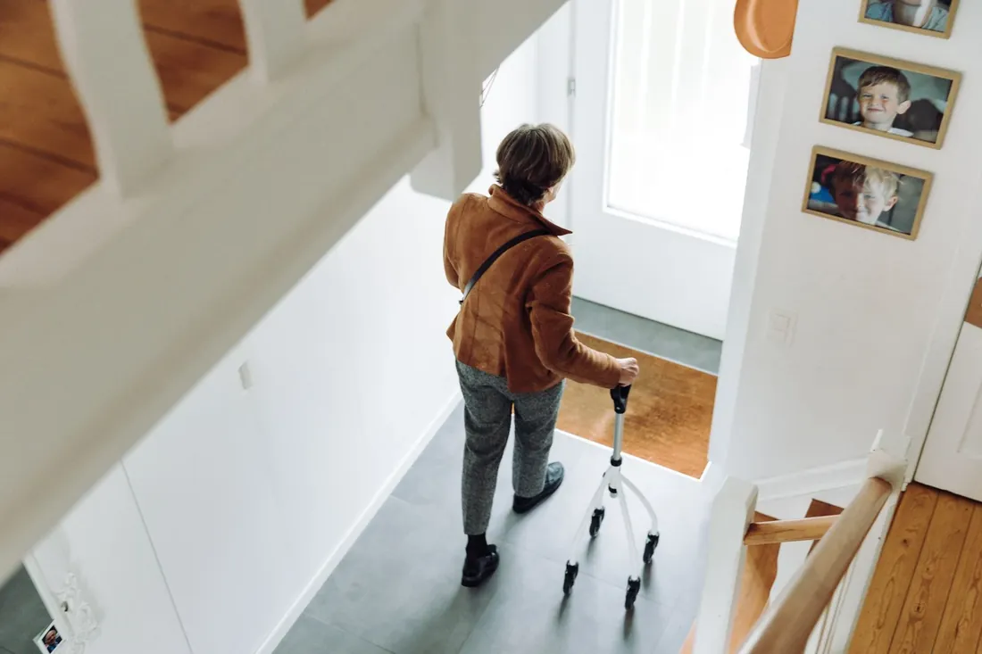 An older woman with a walking stick at the foot of her stairs