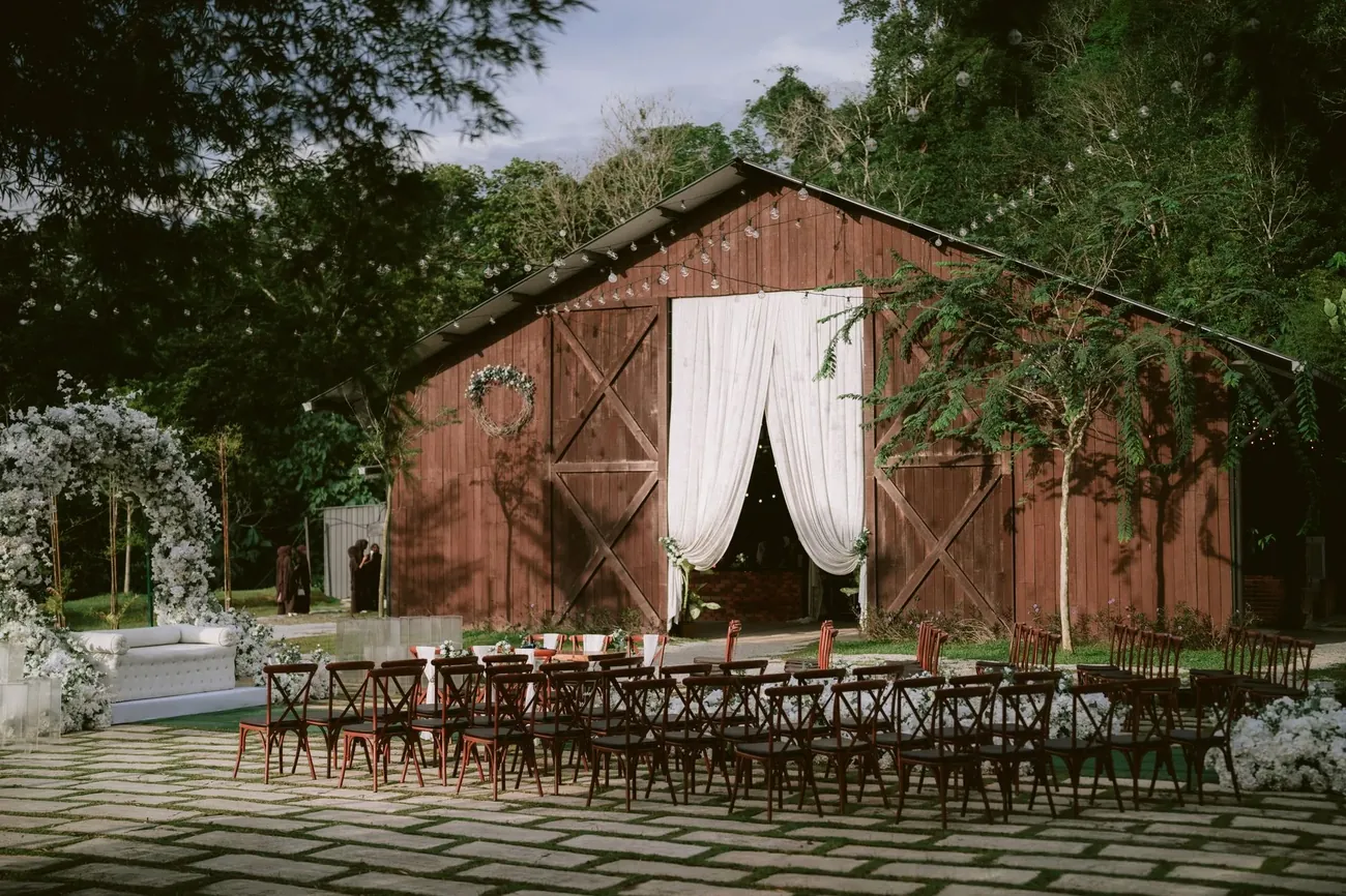 A timber barn at dusk with white drapes at the door and rows of wooden chairs