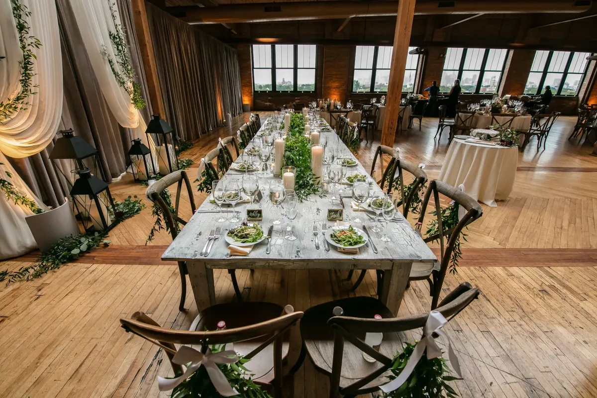 Long wooden tables set for dinner in a barn with oak floors and tall windows