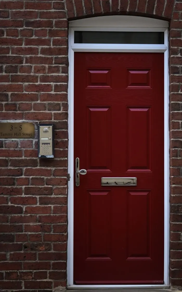 A red panelled front door in a brick terrace