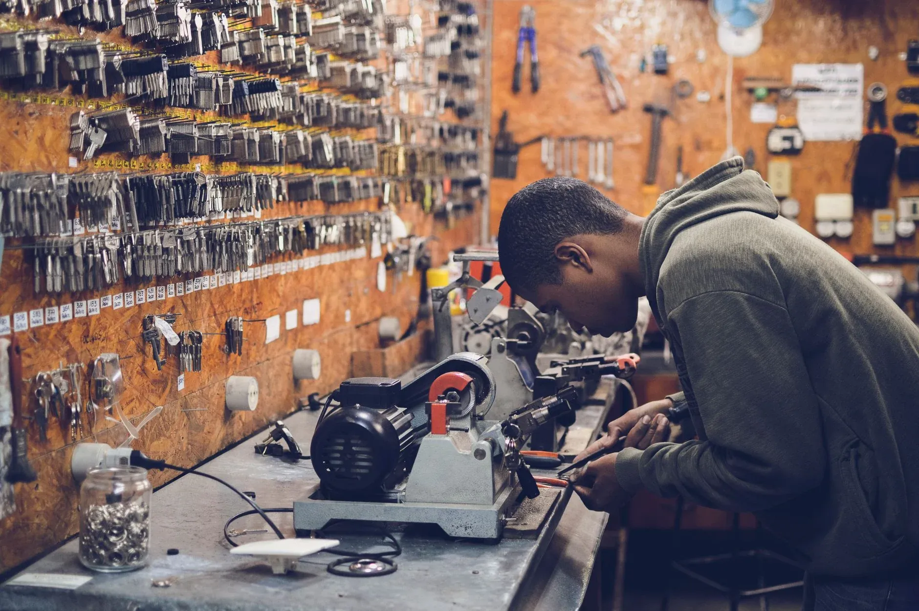 A Latchkey locksmith cutting a key at the bench, a wall of key blanks behind him