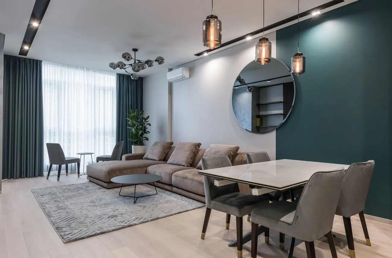 A bright open plan flat with a grey sofa, a dining table and a deep green feature wall