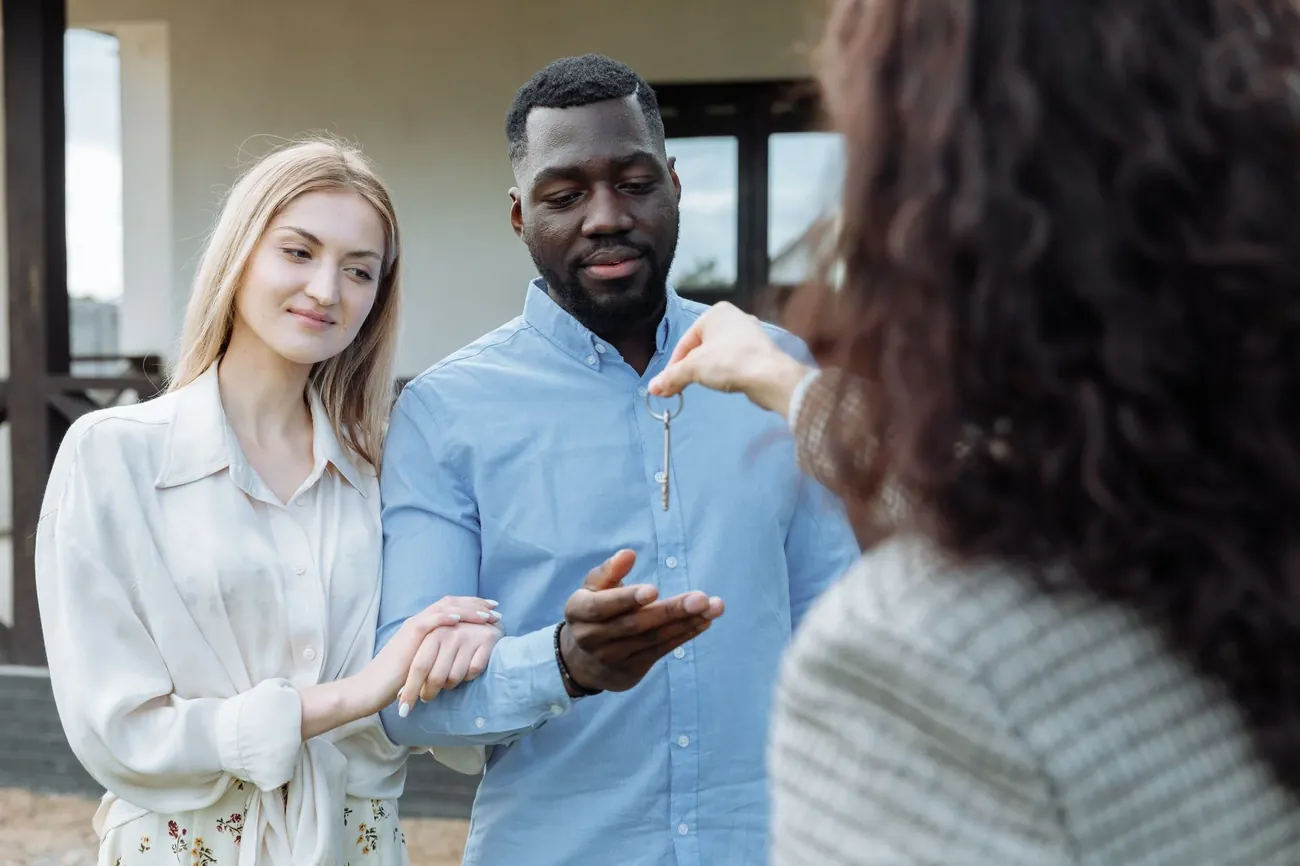 A letting agent handing keys to a smiling couple in a bright living room