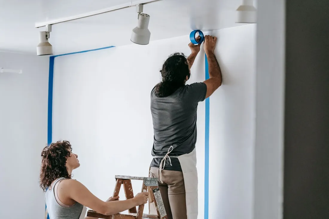 Two decorators taping and painting a white wall in a flat