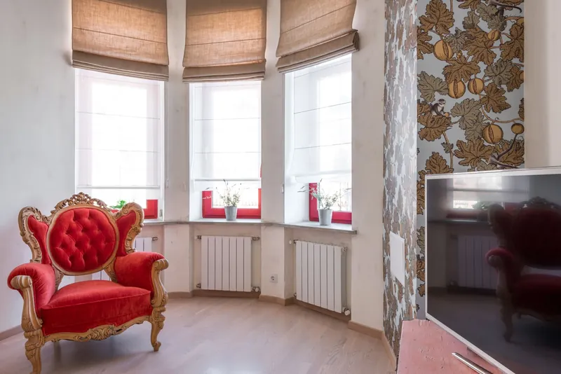 A bay window with soft Roman blinds above a red armchair