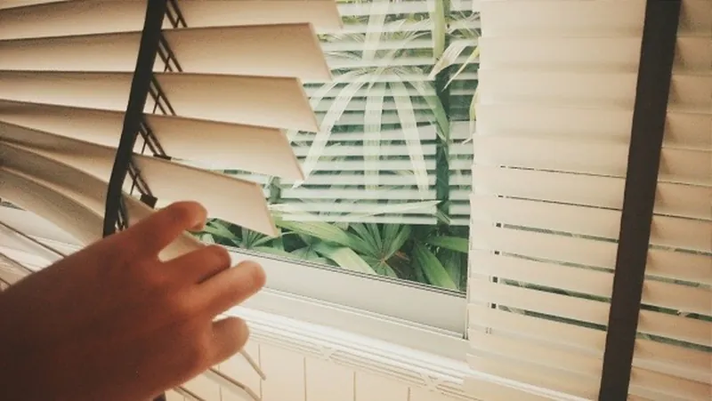A hand tilting the slats of a wooden venetian blind
