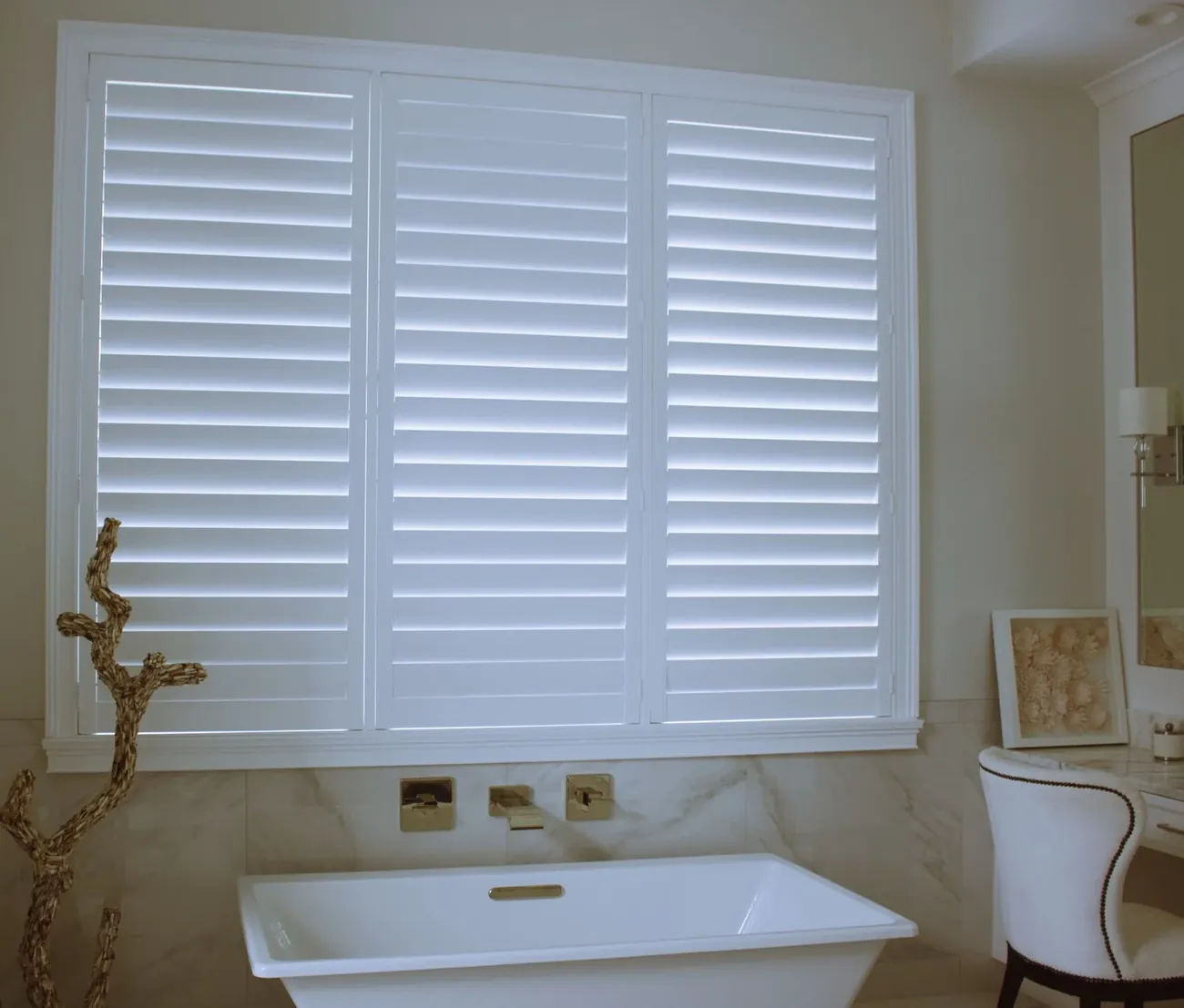 White plantation shutters closed over a window beside a freestanding bath