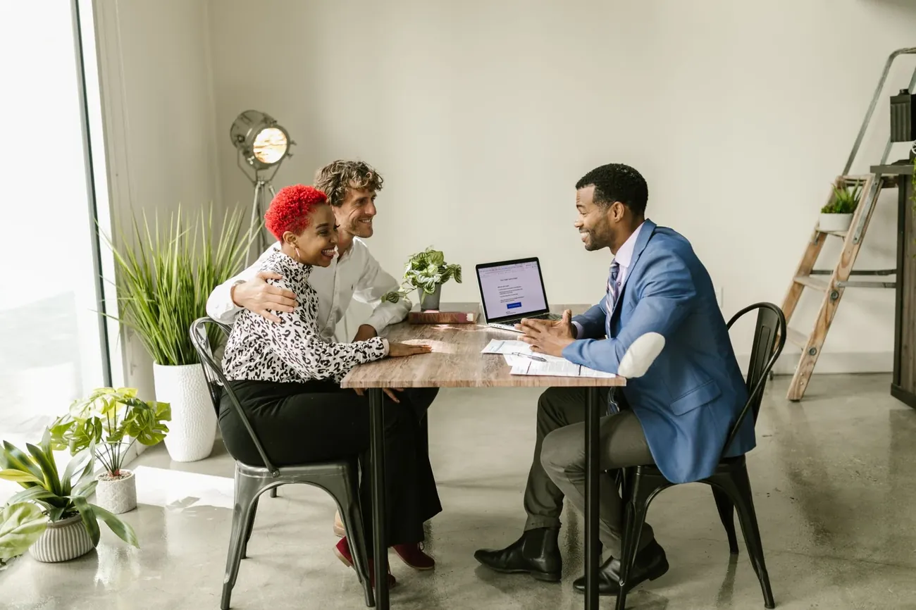 A broker talking through options with two clients at a table in a bright office