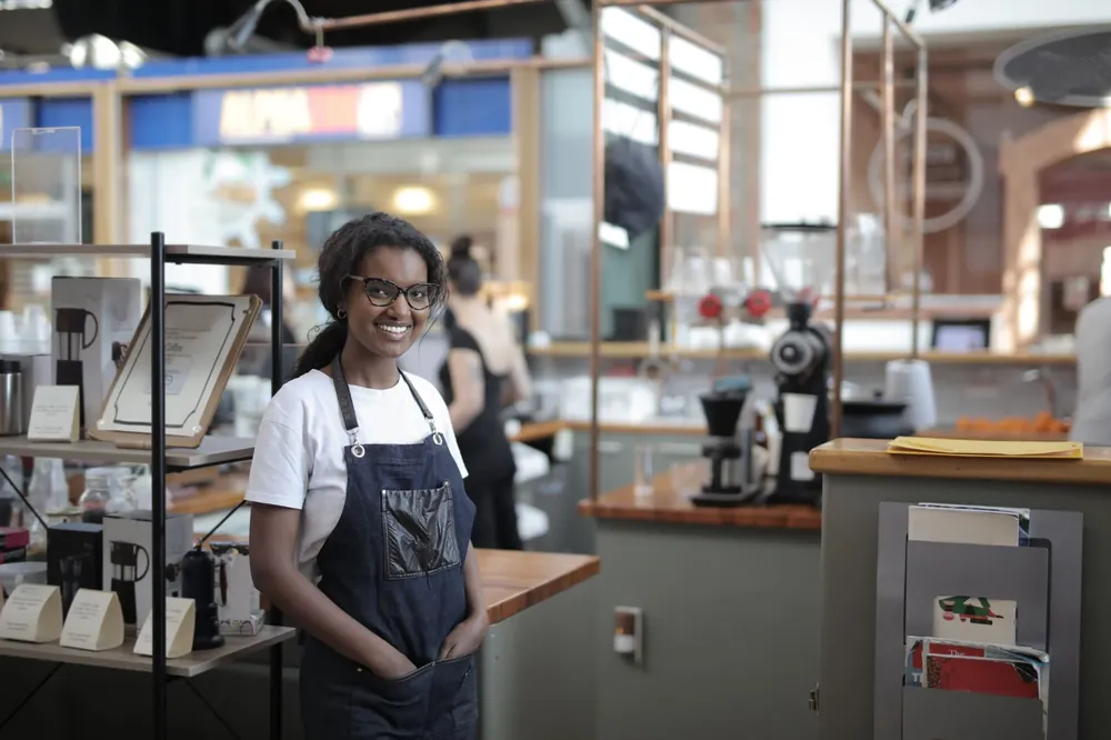 A smiling cafe owner in a denim apron beside the coffee machine