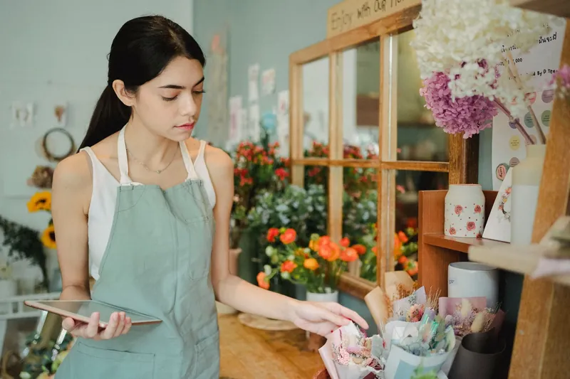 A florist in a green apron wrapping a bouquet in her shop