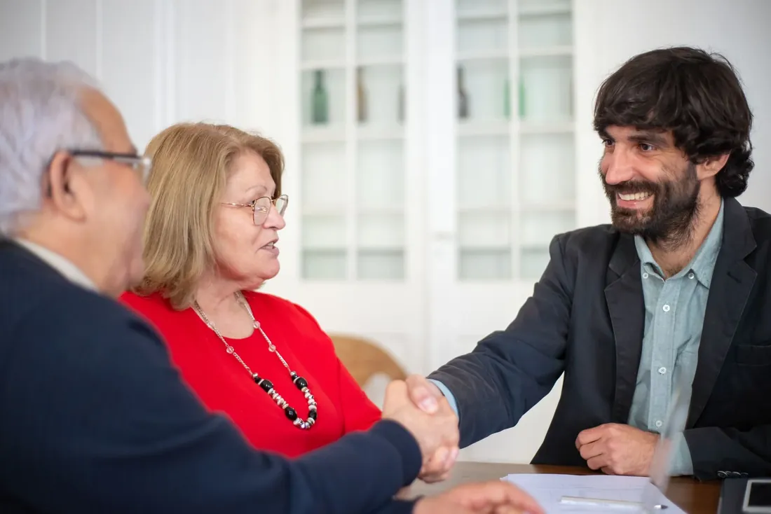 A broker shaking hands with an older couple across a desk