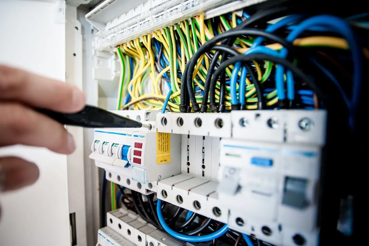 An electrician tightening a terminal in a consumer unit, brown and blue cables in view