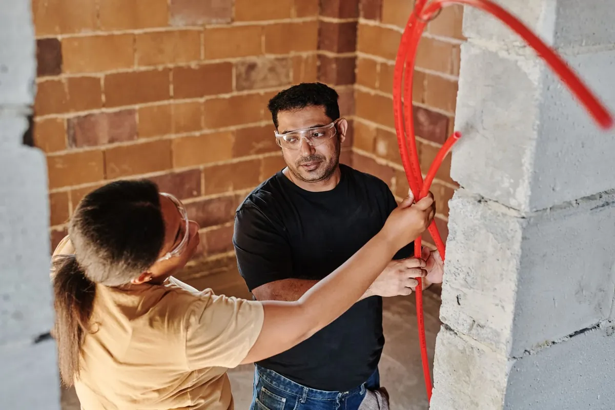 Two electricians pulling new cable through a brick wall during a rewire
