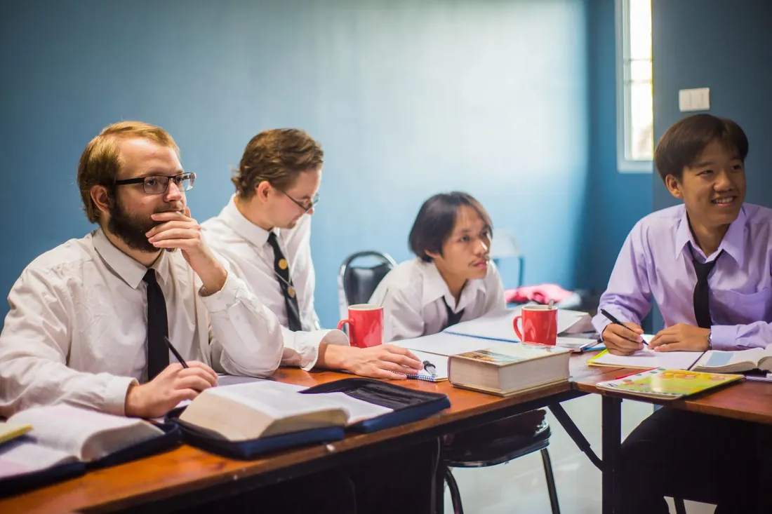 A tutor and a small group of students in school uniform working at a table